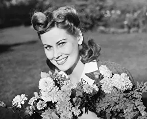 Woman in yard holding bunch of flowers, (B&W), portrait