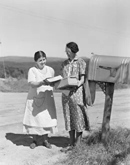 Two women collect mail from country mailbox