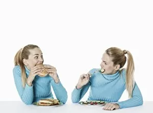 Images Dated 20th February 2013: Two women eating food, one eating fast food, the other one eating uncooked vegetarian food