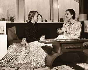 Two Women Sitting on Sofa with Drinks, Chatting