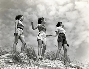 Three women standing on beach, holding hands, smiling. (Photo by H