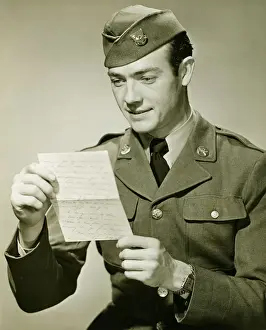 World War II Army solider reading letter in studio, (B&W), portrait