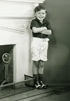 Hearth Prints: Young boy (6-7) standing by fireplace, (B&W)