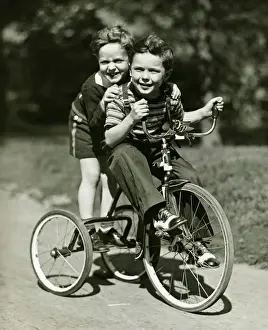 Tricycle Prints: Two young boys (6-7) riding tricycle in park, (B&W), portrait
