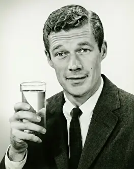 Shirt And Tie Prints: Young businessman holding glass of water, posing in studio, (B&W), portrait