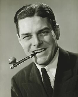 Images Dated 5th May 2006: Young businessman in studio holding pipe in teeth, smiling, (B&W), portrait