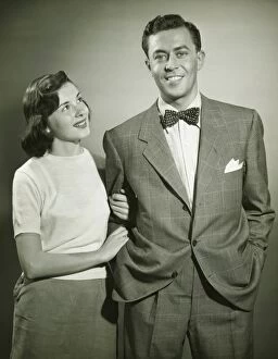 Arm In Arm Gallery: Young couple arm in arm in studio, woman looking at man, smiling, (B&W)