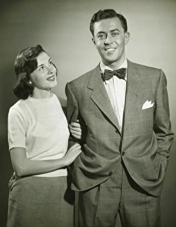 Arm In Arm Gallery: Young couple arm in arm in studio, woman looking at man, smiling, (B&W)