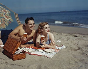 Love Collection: Young couple lying on beach with beer, smiling