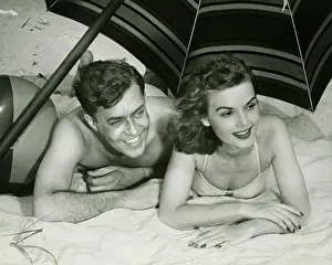Side By Side Prints: Young couple lying on sand under umbrella, smiling, (B&W)