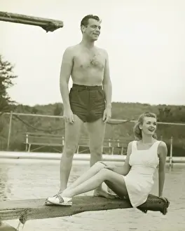 Springboard Prints: Young couple on springboard, man standing, woman sitting, (B&W)