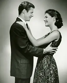 Sundress Prints: Young couple standing face to face, smiling, in studio, (B&W)