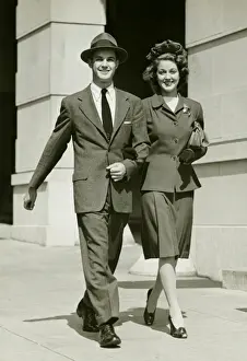 Strolling Prints: Young couple walking arm in arm on sidewalk, (B&W)