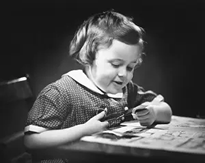 Only Girls Prints: Young girl (4-5) at table cutting paper with scissors, (B&W), close-up