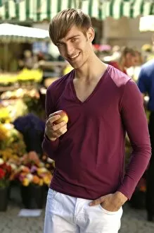 Nourishment Collection: Young happy man holding an apple at a market