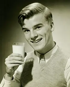 Jumper Prints: Young man holding glass of milk, smiling, (B&W), portrait