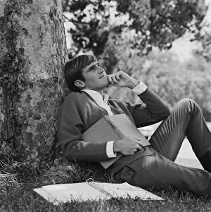Images Dated 20th July 2011: Young man leaning against tree, holding book
