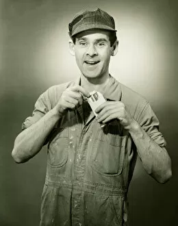 Bib Overalls Gallery: Young man in overalls showing card in studio, (B&W), portrait