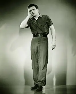 Sleeve Prints: Young man standing in studio, holding hand on forehead, (B&W)