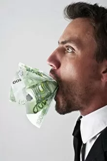 Images Dated 15th August 2012: Young man wearing a suit with 100-euro notes stuffed into his mouth
