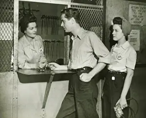 Coworker Prints: Young man and woman returning tools at tool room window, (B&W)