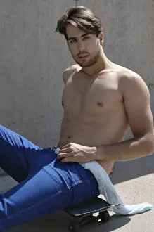 Assurance Prints: Young shirtless skater in front of a concrete wall, sitting on his skateboard