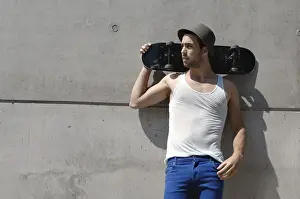 Leans Prints: Young skateboarder standing in front of a concrete wall