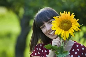 Images Dated 12th July 2011: Young woman, 25, holding a sunflower in front of her face