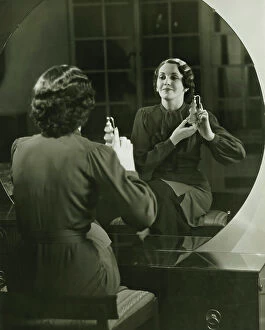 Images Dated 3rd May 2006: Young woman applying perfume in front of mirror, (B&W)