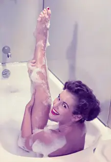 Young woman in bath tub lathering raised leg, portrait