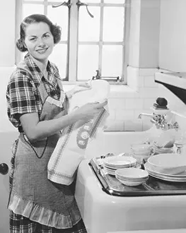 Chores Prints: Young woman drying dishes in kitchen (B&W), portrait