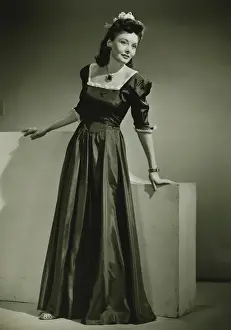 Black Colour Prints: Young woman in evening dress leaning against low wall indoors, (B&W)