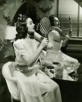 Young woman examining make-up in mirror, (B&W)
