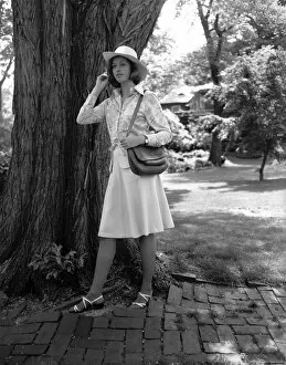 1960s Fashion Gallery: Young woman in hat standing by tree, (B&W)