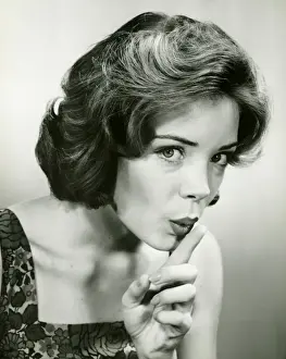 Whispering Prints: Young woman holding finger on lips, posing in studio, (B&W), (Portrait)