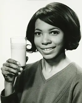 Healthy Style Prints: Young woman holding glass of milk in studio, smiling, (B&W), portrait