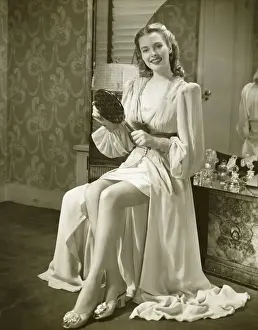 Young woman holding mirror, sitting at dresser, (B&W)