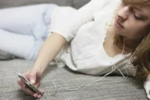 Introspection Prints: Young woman lying on a sofa with an MP3 player, listening to music through headphones