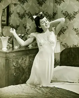 Hand Prints: Young woman in nightgown kneeling on bed, (B&W)