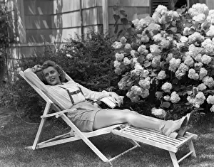 Bushes Prints: Young woman relaxing in deckchair in garden