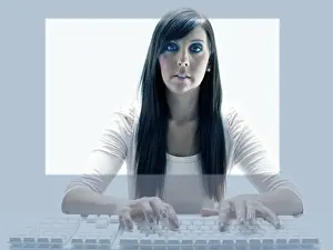 Typing Prints: Young woman seen through the display of a computer while using the keyboard