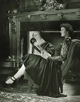 Quality Time Prints: Young woman sitting by fireplace, holding album, (B&W)