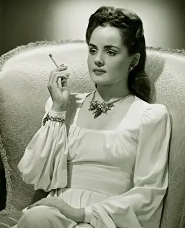 Smoking Activity Prints: Young woman sitting in stylish armchair, smoking, (B&W)