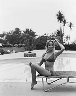 Iconic Bikini Collection: Young woman sitting on sun lounger by swimming pool, smiling, portrait