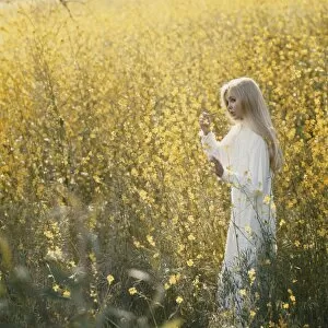 Young woman standing in field holding flower