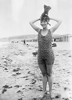 Young woman standing in sandy beach with dog on top of head