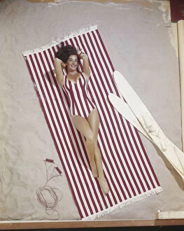 Young woman in striped swimwear lying on striped blanket