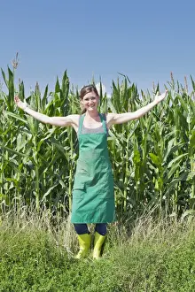 Corn Prints: Young woman in work clothes standing with outstretched arms in front of a maize field